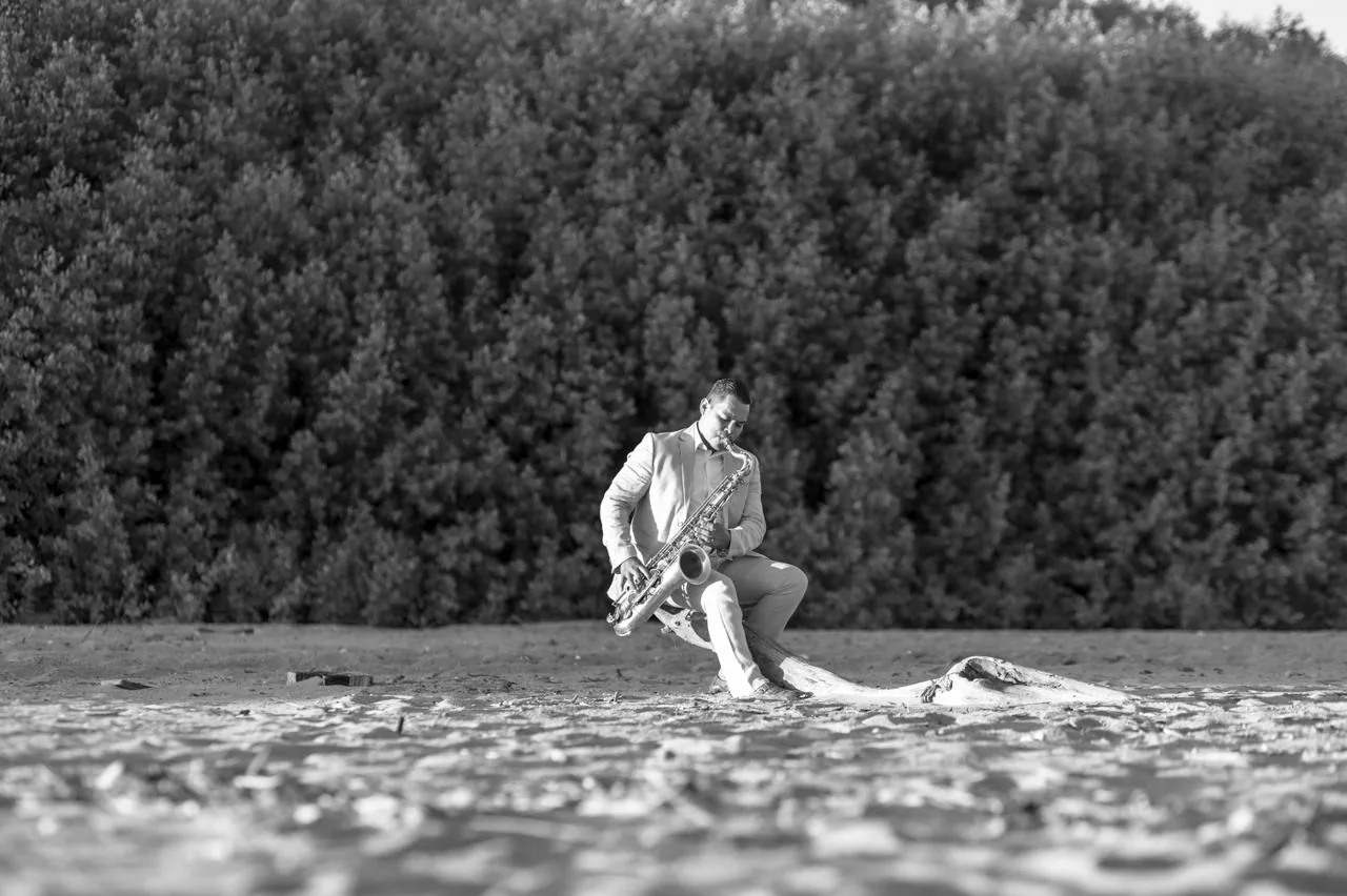 Aleicy Flores tocando saxofón en paisaje de playa en blanco y negro